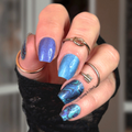 Hand with blue nail polish wraps and multiple rings against a blurred background