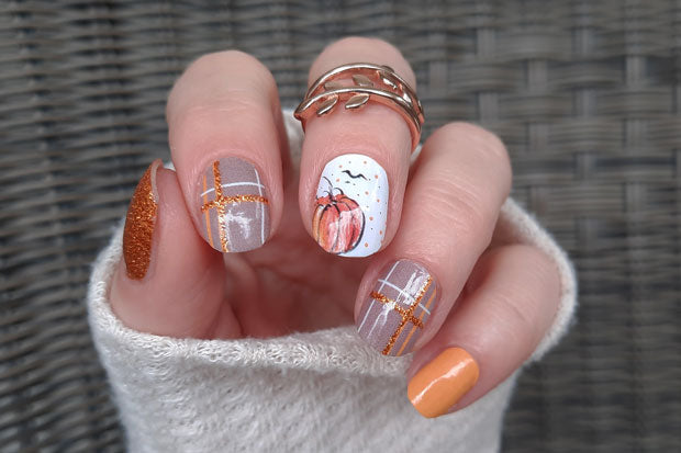 A set of nail wraps featuring pumpkin motifs and a shimmering orange glitter design, displayed on a person's hand with a manicure look.