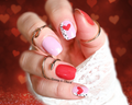 Close-up of a hand with pink and red nail polish wraps on a heart-themed background