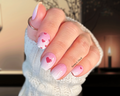 Hand with pink nail polish stickers featuring heart designs, wearing a white textured sleeve.