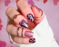 Hand with pink glittery nails and black heart designs on a pink heart patterned background
