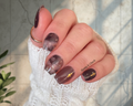 Hand with grey navy and gold foil nail polish and gold accents on a blurred background