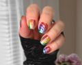 Hand with multicolored glittery nail polish strips against a neutral background