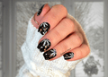 Hand with black and white snowflake nail wrap design wearing a white textured sweater.