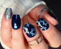 Nail art with blue wrpas and star designs on a hand wearing rings.