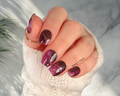 Hand with black and purple glittery nail stickers wearing a white textured sleeve.