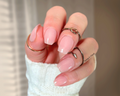 Close-up of a hand with sheer pink nail stickers and multiple rings on a neutral background