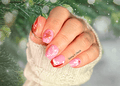Hand with pink and red Christmas themed nail wraps with a blurred green background
