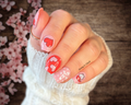 Hand with pink and red nail stickers on a wooden surface with cherry blossoms.