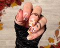 Hand with autumn-themed thanksgiving nail art stickers against a leafy background