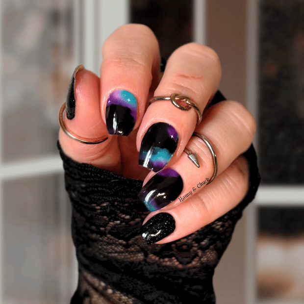 Close-up of a hand with black and purple nail strips wearing a black lace glove.