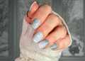 Close-up of a hand with greenish-gray and silver winter themed nail art design, wearing a white textured sleeve.