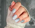Close-up of a hand with greenish-gray and silver winter themed nail art design, wearing a white textured sleeve.