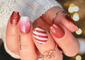 Close-up of a hand with decorated nail wraps featuring red, white, and glitter designs.