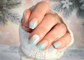 Hand with light aqua and peach gradient nail wraps with snowflake designs against a blurred natural background
