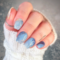 Hand with blue and silver marble nail wraps against a gray background
