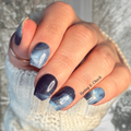 Hand with blue and gold marbled nail wrap design, wearing a textured white sleeve.