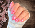Hand with pink nail stickers featuring heart designs, wearing a white sleeve, against a wooden background with cherry blossoms.