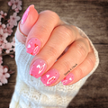 Hand with pink nail polish wraps featuring heart designs, wearing a white sleeve, against a wooden background with cherry blossoms.
