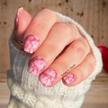 Hand with pink hearts nail wrap design wearing a white sleeve against a wooden background