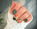 Nail wraps on a hand with festive designs, including a rainbow, pot of gold, and leprechaun.