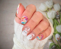 Hand with Easter-themed nail art featuring bunnies and rainbows, with tulips in the background.