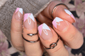 Close-up of a hand with pink and white nail art on a blurred floral background