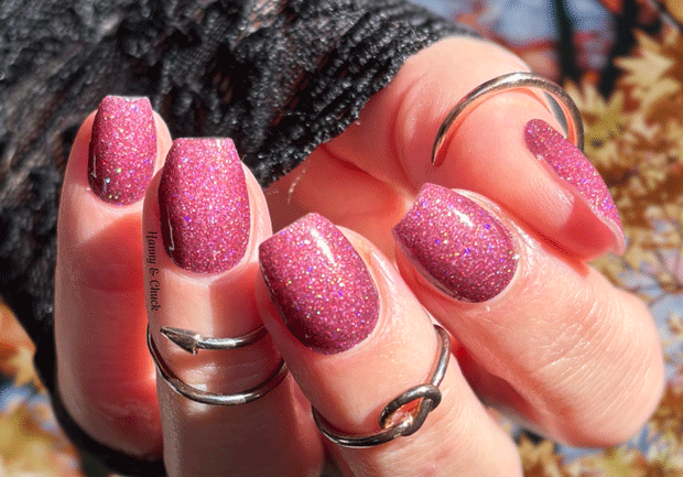 Close-up of a hand with pink glittery nail wraps and multiple silver rings.