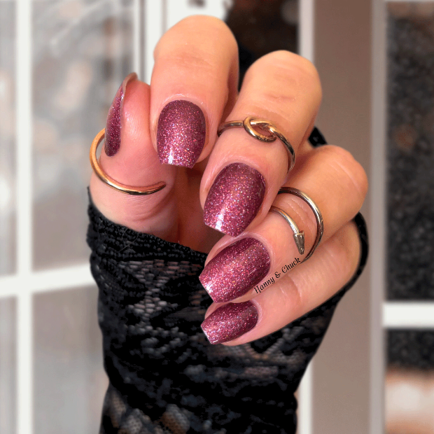 Hand with glittery burgundy nail polish wraps wearing black fingerless gloves.