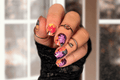 Hand with colorful autumn themed nail wrap art wearing black lace gloves against a blurred indoor background