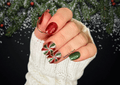 Hand with festive green, red and pink nail art stickers against a snowy background