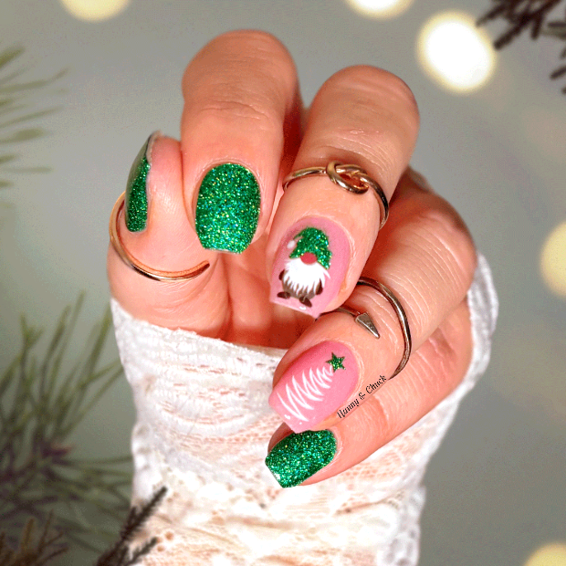 Hand with festive green and pink gnome nail art stickers in front of a blurred Christmas-themed background