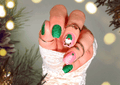 Hand with festive pink and green gnome nail art stickers against a blurred Christmas-themed background