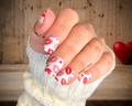 Hand with red and white kissing lips nail design holding a heart-shaped object against a wooden background