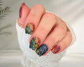 Hand with rainbow clover glitter nail wraps on a blurred background