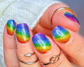 A close-up image of a person's fingernails, which are adorned with vibrant rainbow stripes glitter nail wraps.