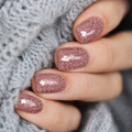 Close-up of rose pink glitter nail wraps on short natural nails against a soft grey knit background.