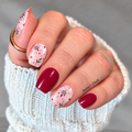 Hand wearing Berry Verity nail wraps with glossy burgundy nails and blush pink accents featuring white flowers, dark leaves and berry-red dots.