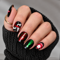 Black Christmas nail wraps with Santa, white reindeer, and red and green metallic Christmas trees on a hand wearing a black sweater.