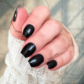 Glossy black nail wraps with fine glitter on short natural nails, subtle sparkle over deep black polish.