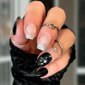 Hand with black and white glittery nail wrap design wearing a black textured sleeve.