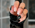 Hand with black and white nail design wearing a black glove against a blurred background