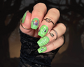 Hand with green  nail art with black cats and multiple rings against a blurred background