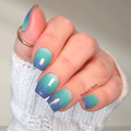 Hand with blue and green gradient nail wraps on a neutral background