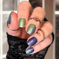 Hand with glittery blue and green nail wraps wearing multiple rings against a blurred background
