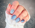 Hand with blue and silver marble nail art stickers against a gray background