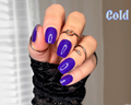 Hand with blue colour change nail wraps wearing black rings against a neutral background