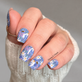 whimsical blue, white, and purple floral nail wraps. A small gold ring is worn on the middle finger, and a watermark 'Hannah & Chuck.