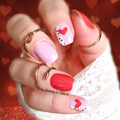 Close-up of a hand with pink and red nail polish wraps on a heart-themed background
