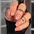 Close-up of a hand with dark cream nail strips and multiple rings against a blurred background